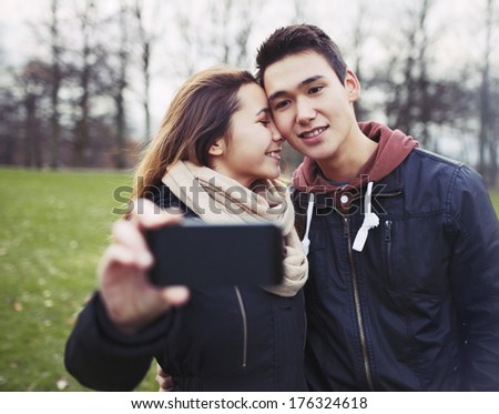 Affectionate young couple taking pictures using a smart phone at the park. Teenage boy and girl in love photographing themselves outdoors.