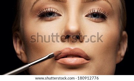 Close up female face with makeup lipstick brush. Young woman applying lip gloss with make up brush on lips. Tight crop.