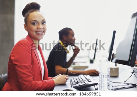 Happy young african american woman sitting in front of computer smiling at camera. Young students sitting at table using computers at school.