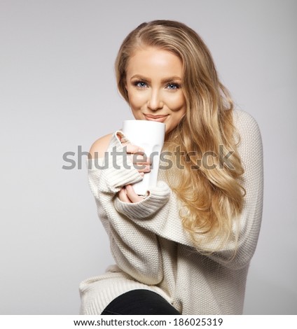 Cute smiling girl in oversized sweater. Lovely smiling young woman holding a cup of warm tea or coffee.