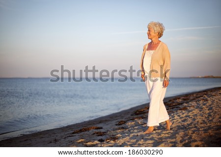 Portrait of a mature woman walking on the beach looking at the sea. Relaxed old lady strolling on the beach with lots of copyspace.