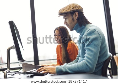 Two young people finding information on internet for their academic project. Students sitting at table with book and computer studying together for exams.