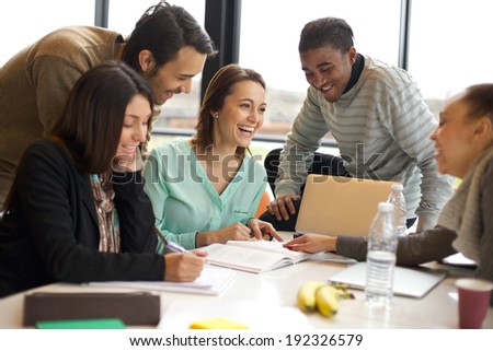 Multiracial young people enjoying group study at table. Happy university students sitting together at table with books and laptop for researching information for their project.