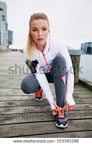 Pretty young woman tying her shoe laces before a run. Fit young female runner training outdoors.