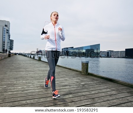 Female runner training outside. Caucasian female athlete jogging on boardwalk along river in city. Fit young woman running.