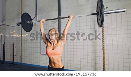 Muscular young woman doing weightlifting at crossfit gym. Fit female model lifting heavy weights at gym.