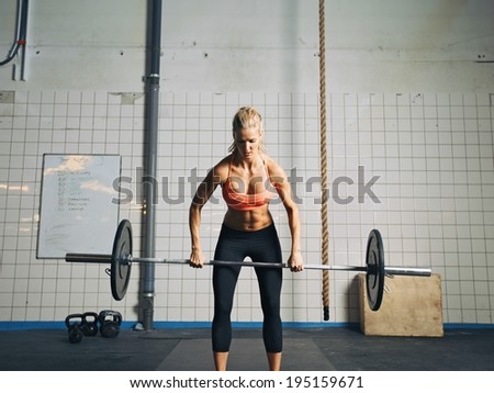 Fit and attractive caucasian female holding a barbell in her hands. Crossfit woman lifting heavy weights in gym.
