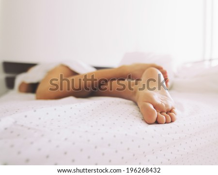 Feet of a woman sleeping in bed at home. Legs of a female lying on bed - Indoors