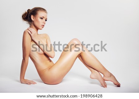 Gorgeous naked lady sitting on floor covering her breast with her hand and looking away in thought. Pensive nude woman sitting on grey background with copyspace.
