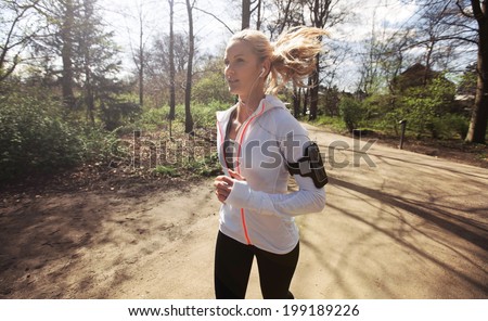 Young woman running in park in sunshine on beautiful summer day. Fitness model training outdoor for good health.