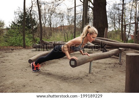 Tough young woman doing pushups on a log at park. Fit young woman exercising in woods.