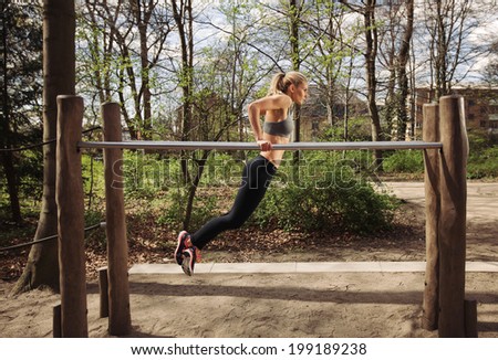 Strong and physically fit young woman doing triceps dips on parallel bars at park. Caucasian fitness female exercising outdoors.
