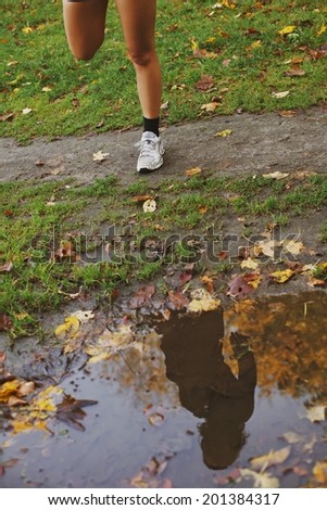 Reflection of young woman in a puddle of water in park. Low section of fitness female legs doing stretching exercise outdoors