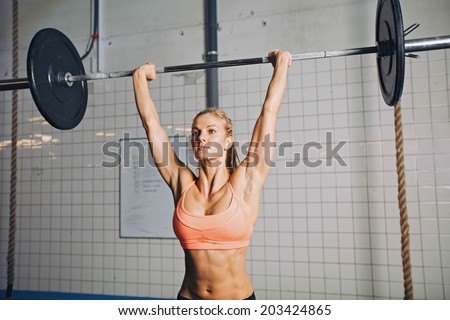 Beautiful strong young woman with barbell and weight plates overhead. Fit young female athlete lifting heavy weights. Caucasian female model performing crossfit exercise.