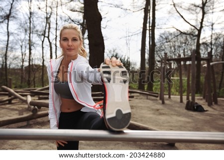 Pretty young female athlete stretching before a run. Young runner stretching her muscles before a training session outdoors in forest.