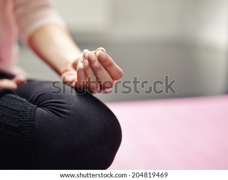 Low section of woman sitting cross-legged on mat meditating in yoga posture. Cropped image of woman practicing yoga with focus on hand.