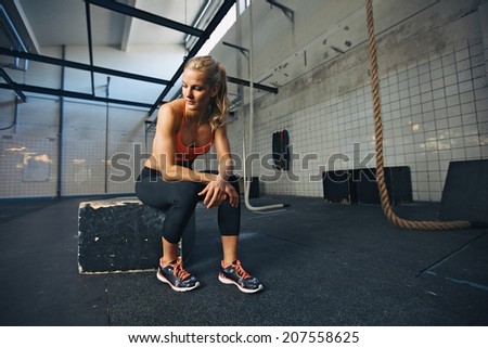 Caucasian female athlete sitting on a box at gym thinking. Fit young woman taking break after her workout at gym.