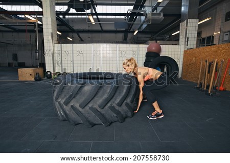 Tough female athlete flipping a huge tire. Young woman doing crossfit exercise at gym.