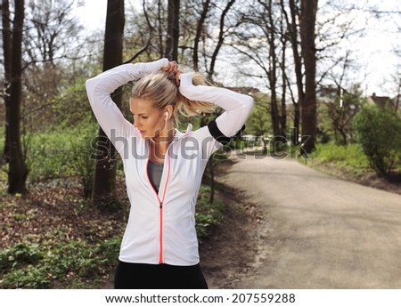 Fit female athlete tying hair before her run. Pretty young woman preparing for her run in forest.