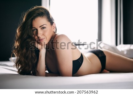 Portrait of sexy female in lingerie lying on front on bed looking at camera. Caucasian woman lying on bed in underwear.