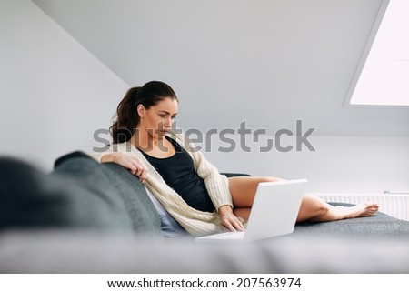 Portrait of relaxed young woman sitting on couch using her laptop. Caucasian female model working on laptop at home.