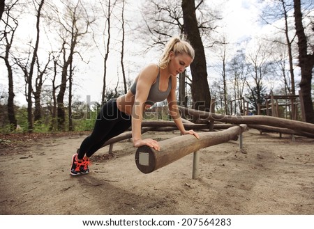 Fit young lady exercising in park. Strong and muscular young female doing pushups on a log.