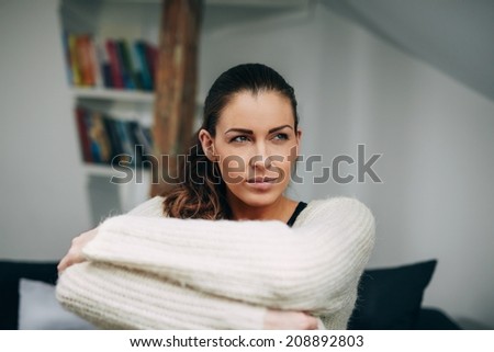 Portrait of young lady sitting alone on sofa looking away. Caucasian female model at home daydreaming.
