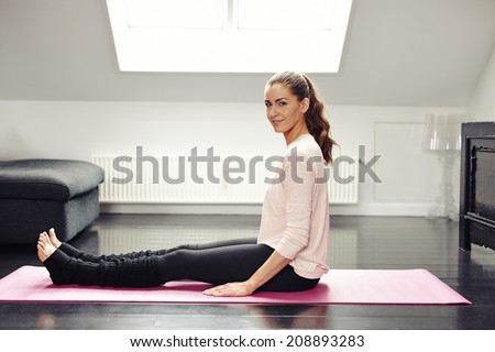 Portrait of fresh young woman sitting on exercise mat looking at camera smiling. Beautiful female exercising in living room.