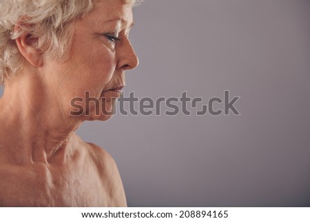 Profile view of senior woman face against grey background, Naked mature woman looking down.