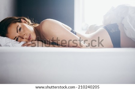 Woman in lingerie lying in her bed looking at camera. Beautiful young woman relaxing in bedroom.