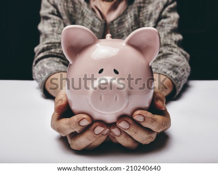 Close-up shot of elderly woman holding pink pig money-box. Senior woman hands holding a piggybank. Concept of saving money for old age.