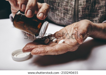Close-up image of senior woman taking out pills from the pills bottle. Focus on hands. Old female taking medicines.