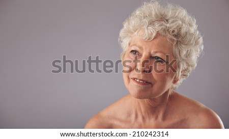 Close-up portrait of attractive senior female looking away in thought. Old woman daydreaming against grey background with copy space for your text.
