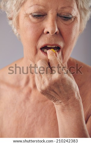 Close-up image of a senior woman taking a pill against grey background. Old female taking medicine.
