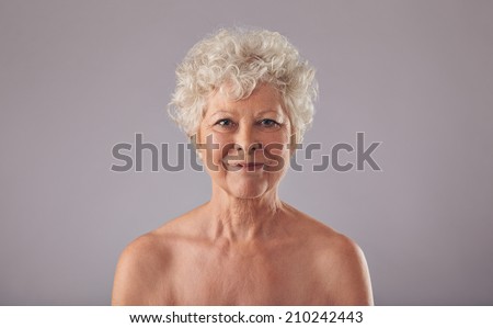 Portrait of beautiful senior woman shirtless against grey background. Naked old woman smiling at camera.