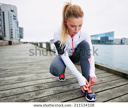 Fit and sporty young woman tying her laces before a run. Female runner tying her shoelaces while training outdoor.