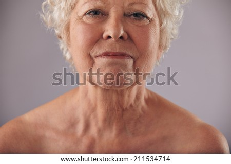 Close-up image of mature woman face with wrinkled skin condition against grey background. Senior woman naked chest and shoulders.