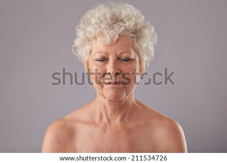 Close-up of relaxed old woman on grey background with her eyes closed in thought. Naked senior female against grey background.