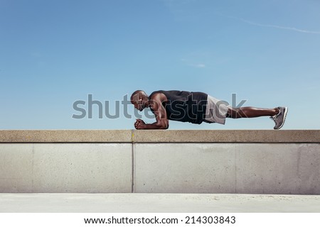 Side view of strong young african athlete doing core exercise on a wall by a walkway. Muscular young athlete exercising outdoors against clear sky. With lots of copy space.