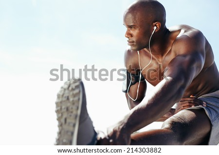 Image of muscular young man working out against sky. African man looking away with stretching his leg. Shirtless male model exercising outdoors.