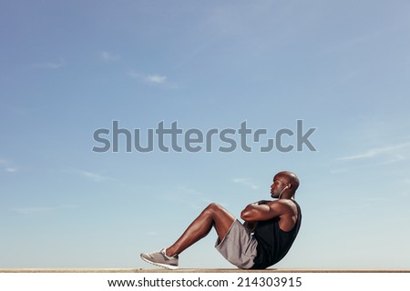 Side view of fitness model doing crunches against blue sky. Young african man doing abdominal exercise outdoors.