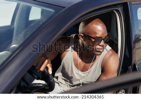 Image of young man in car looking away. Stylish african guy on road trip.