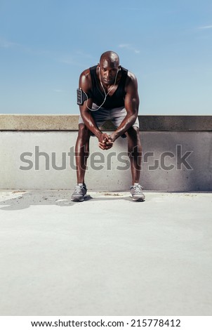 Portrait of a exhausted runner sitting outdoors. Muscular and fit young athlete relaxing after his fitness training.