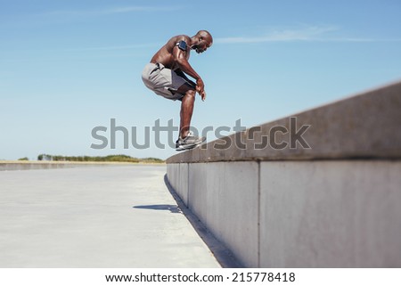 Image of shirtless young athlete jumping from a wall. African fitness male model doing jump exercise outdoors.
