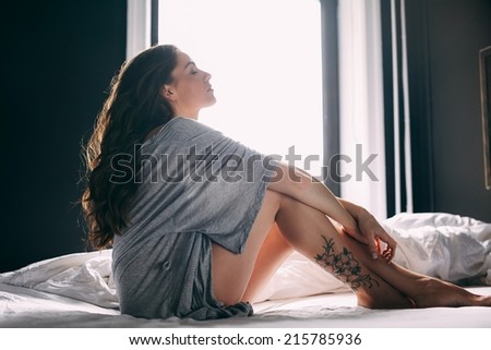 Side view of woman sitting relaxed on bed with her eyes closed. Relaxed female in bedroom.