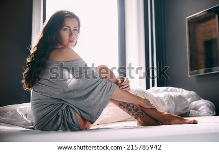 Portrait of beautiful young lady sitting on bed. Caucasian female model in nightwear in bedroom.