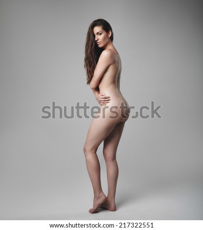 Full length hot young woman posing sensually over grey background, Naked female model covering her breast with her hands.