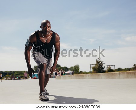 Fit young man on his mark to start running. Determined athlete outdoors. Muscular african male model ready for his run on a hot summer day.