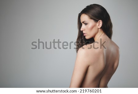 Topless woman against grey background. Naked female model with blank expression.