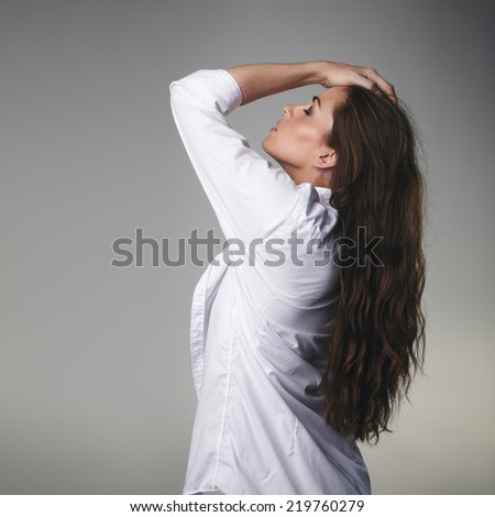 Image of passionate young brunette posing with her hands in hair against grey background